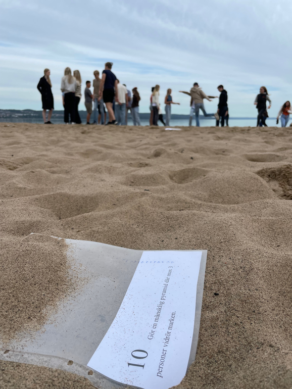 Vätterstranden med en papperslapp i förgrunden och en klass elever i bakgrunden.