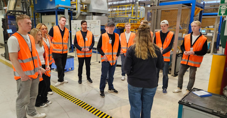 Elever som står i orangea varselvästar och lyssnar på en representant från Husqvarna AB.