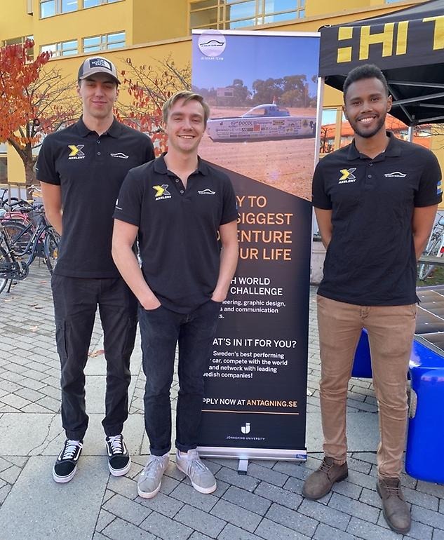 Tre elever från JTH framför en roll-up med reklam för JU Solar Challange.